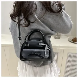 Detailed view of black mini crossbody bag with leather bow and plaid ribbon accent