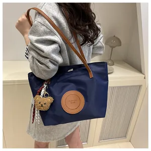 Detail of navy tote bag with brown handles and cute bear charm shown on model