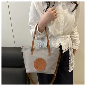 Detail of grey tote bag showing nylon texture with brown leather handles and shoulder strap