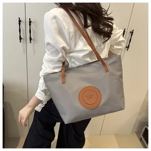 Close-up of a large grey nylon tote bag with brown faux leather straps and fashion patch