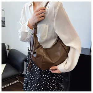 Close-up of a dark brown pleated PU leather crescent bag with knot and tassel details