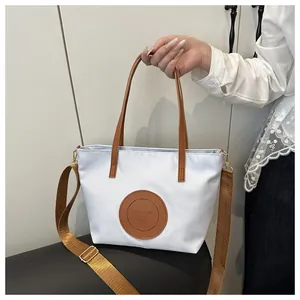 Detail of white tote bag with brown leather handles and adjustable woven shoulder strap