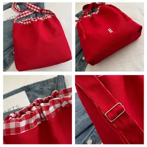 Detail of red canvas bucket bag showing checkered trim and adjustable metal strap buckle
