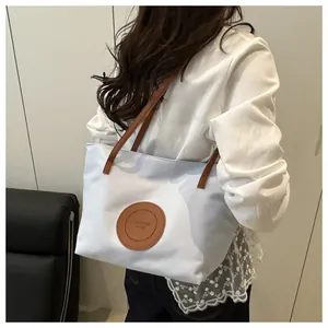 Close-up of white tote bag with brown leather handles and central fashion brand patch