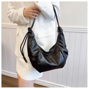 Detail of black pleated hobo bag with knotted strap on a woman in a white blazer