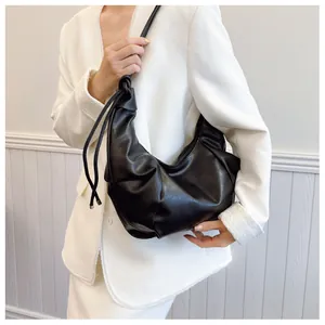 Detail of black pleated hobo bag in soft leather texture on white blazer background