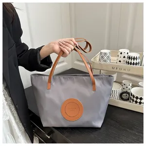 Gray nylon tote bag with brown leather handles and embossed fashion logo on a black counter