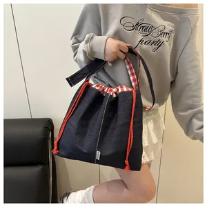 Detail of blue denim crossbody bag with red checkered lining and orange drawstring strap