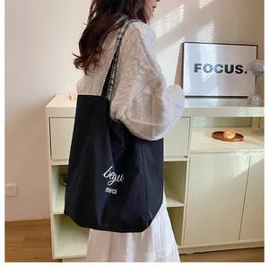 Détail du sac cabas en toile noire avec typographie et bandoulière à motif de carreaux