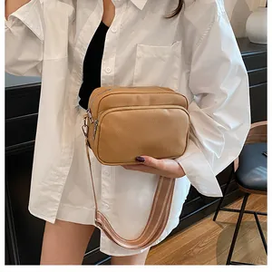 Litchi texture leather crossbody bag with dual zippers and striped wide strap worn by model