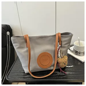 Detail of light gray tote bag with leather logo patch and brown plush bear charm