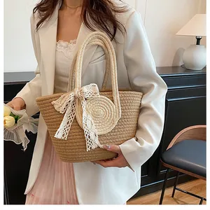 Detail der handgewebten Strohtasche mit eleganter Spitzenschleife und rundem Aufnäher