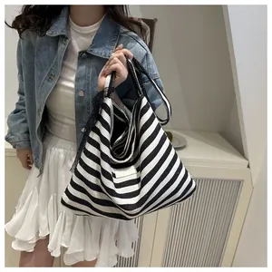 Close-up of a large black and white striped tote bag held by a model in casual attire