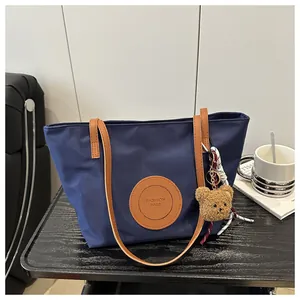 Detail of navy nylon tote bag featuring brown leather logo patch and cute bear keychain