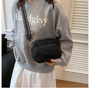 Detailed view of black pebbled leather crossbody bag with striped wide woven shoulder strap