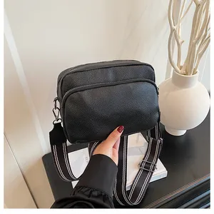 Detail of black pebbled leather crossbody bag with dual zippers and wide striped strap