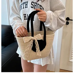 Detail der gewebten Stroh-Tasche mit cremefarbener Spitzenschleife und schwarzen Rundgriffen