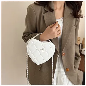 Detail of cream heart-shaped quilted mini bag with pearl handle and metal bow decoration
