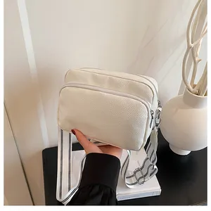 Detail of white pebbled leather crossbody bag with dual zippers and striped strap