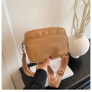 Detail of khaki pebbled leather crossbody bag with wide stripe strap and dual zippers