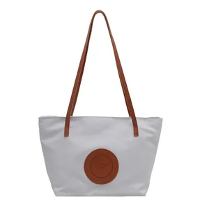 White nylon tote bag with brown leather handles and fashion circular logo patch