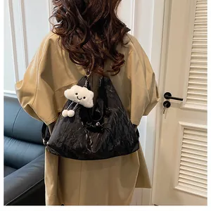 Détail d'un sac cabas noir brillant avec breloque nuage porté avec un trench-coat kaki