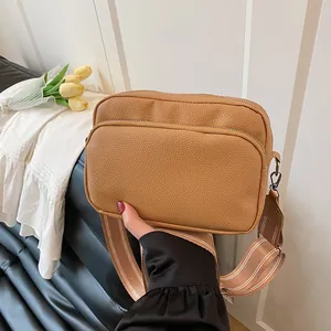 Brown litchi texture crossbody bag with wide striped fabric strap in a modern setting