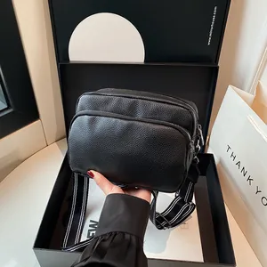 Black pebbled leather crossbody camera bag with striped strap in a luxury gift box