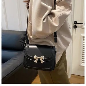 Dettaglio di una borsa a tracolla nera con fibbia a fiocco argento su pelle opaca