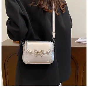 Dettaglio di una borsa a tracolla argento metallizzato con fiocco decorativo su blazer nero