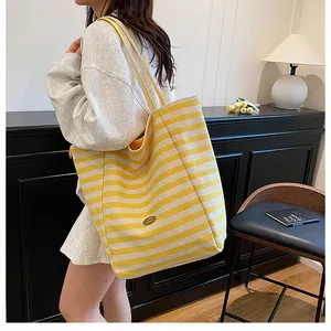 Détail du sac fourre-tout en tricot rayé jaune et blanc avec bandoulières et logo métal