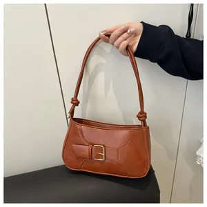 Détail du sac à bandoulière marron en cuir avec boucle en métal et design de nœud sur l'anse