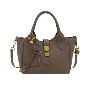 Taupe handtas met lychee-patroon, gouden sluiting en beer-hanger op wit