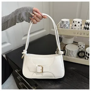 Détail du sac baguette blanc montrant boucle dorée, texture mate et sangle nouée