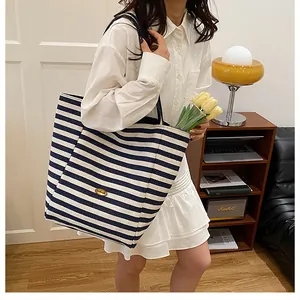 Détail d'un grand sac cabas à rayures bleues et blanches avec logo en métal doré