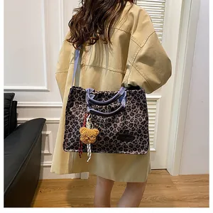 Detail of leopard print canvas tote bag with plush bear charm on a beige coat model
