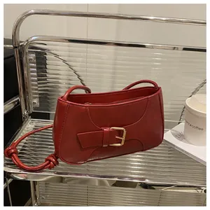 Détail du sac sous l'aisselle en cuir rouge avec bandoulière nouée et boucle dorée