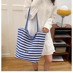 Détail du cabas en toile à rayures bleues et blanches avec logo en métal doré et anses