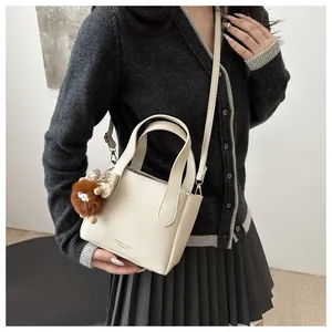 Detalle de bolso tipo cubo de cuero beige con colgante de oso y lazo decorativo