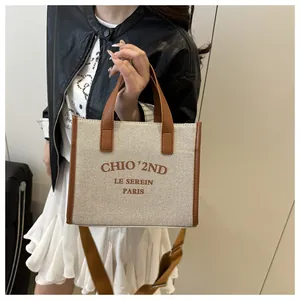 Gros plan du sac en toile beige avec finitions en cuir marron et lettrage imprimé chic