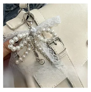 Dettaglio ciondolo a fiocco in perle e pizzo con cuore d'argento su borsa bianca