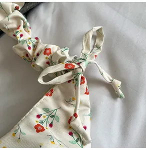 Close-up of beige floral canvas dumpling bag with ruched strap and bow detail decor