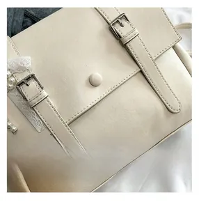 Dettaglio ravvicinato della borsa in pelle crema con bordo in pizzo e ciondolo di perline