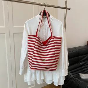 Grand sac cabas en maille rayé rouge et blanc avec logo doré sur fond de chemise blanche
