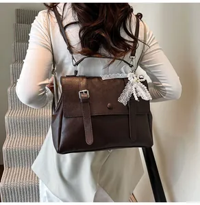 Detail of dark brown leather backpack with lace bow and pearl charm on white top