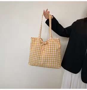 Detail of yellow gingham tote bag with a small bow knot accent worn by a model
