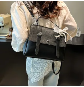 Close-up of black matte leather shoulder bag with white lace pearl bow and metal buckle