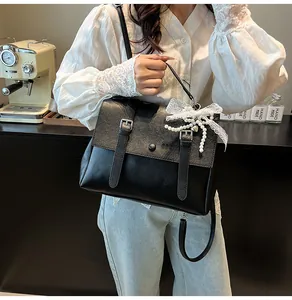Dettaglio borsa nera in ecopelle con fiocco di pizzo bianco e ciondolo di perle eleganti