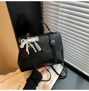 Detail of black leather handbag with white lace bow pearl charm and metal buckles