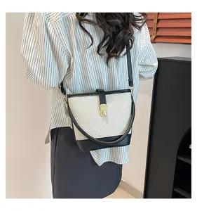 Detail of contrast stitching and golden twist lock on woven ivory bucket bag